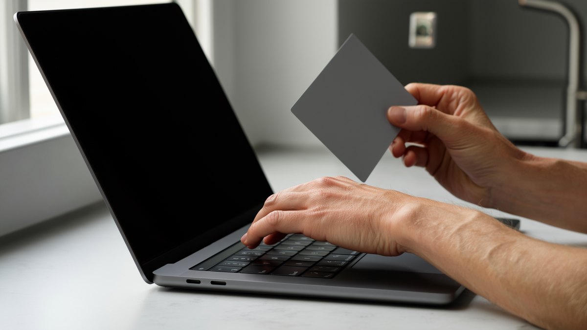 A player holding a payment card over a laptop keyboard at a kitchen table