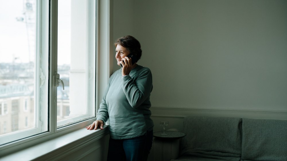 A woman standing by a window making a call to a problem-gambling helpline